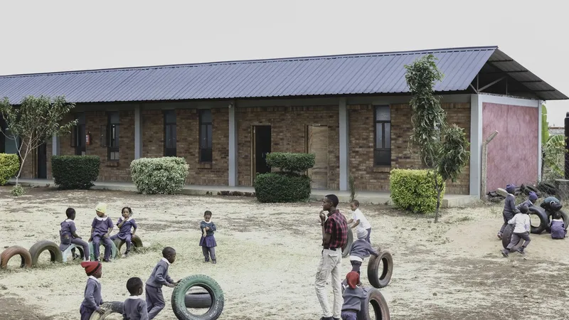 Brick facade with metal roof and planted courtyard where children play among recycled tire seats