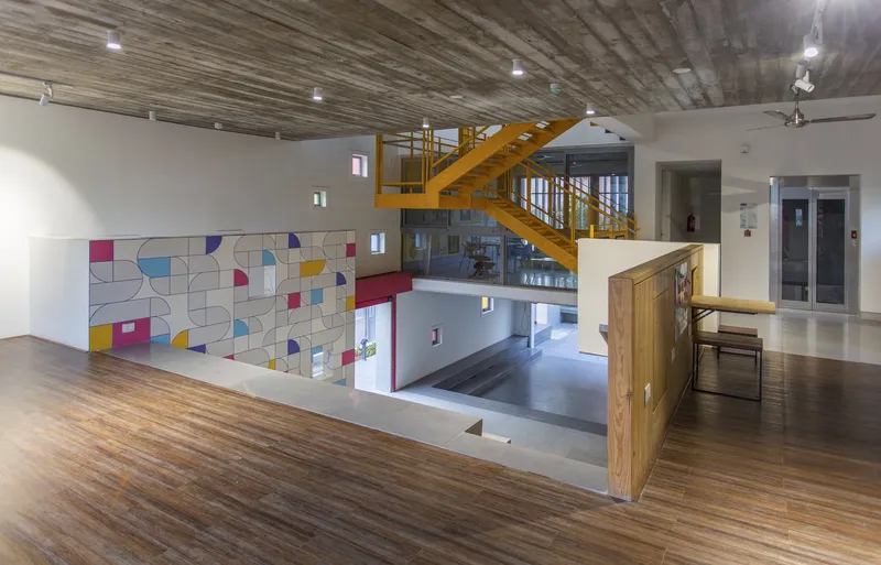 Upper level interior showing yellow steel staircase, timber flooring, and geometric tile mural on the lower wall