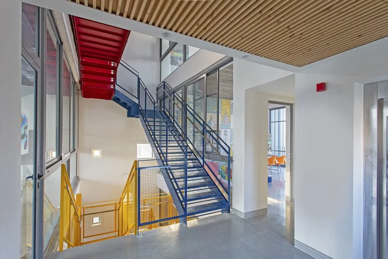 Interior stairwell with metal stairs in yellow and red beneath a slatted timber ceiling