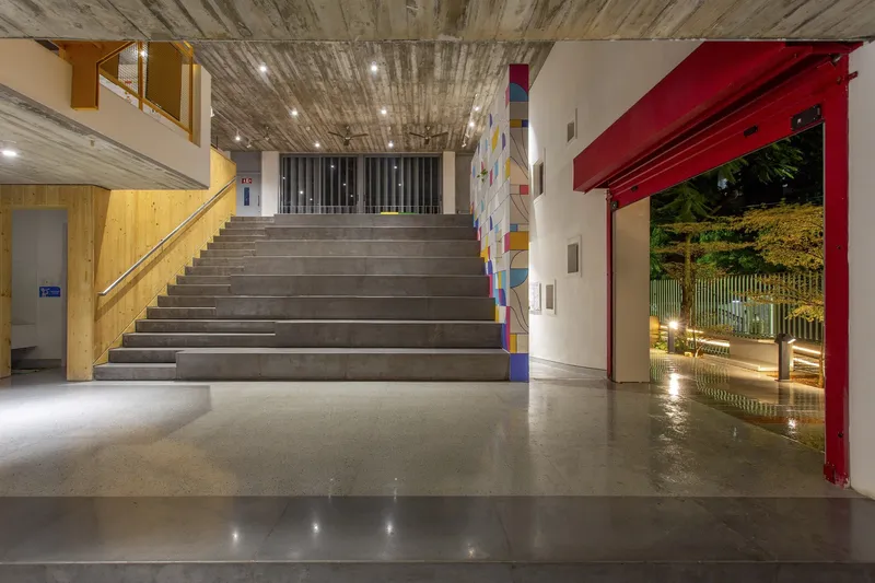 Interior lobby with wide concrete staircase, red roll-up door opening to the street, and exposed timber ceiling at dusk