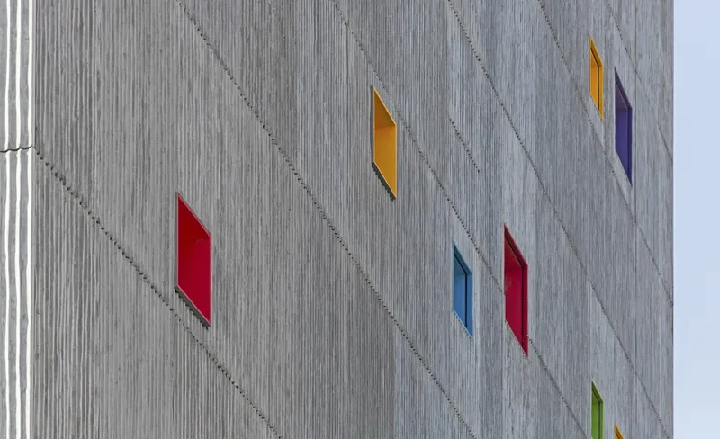 Concrete facade with vertically ribbed panels and colored diamond-shaped window openings in red, yellow, and purple