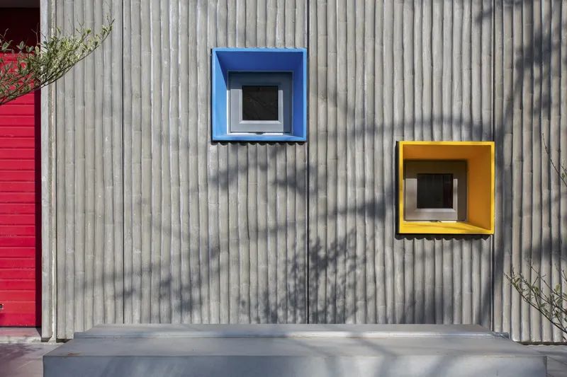 Corrugated metal wall with blue and yellow framed windows casting shadows in sunlight
