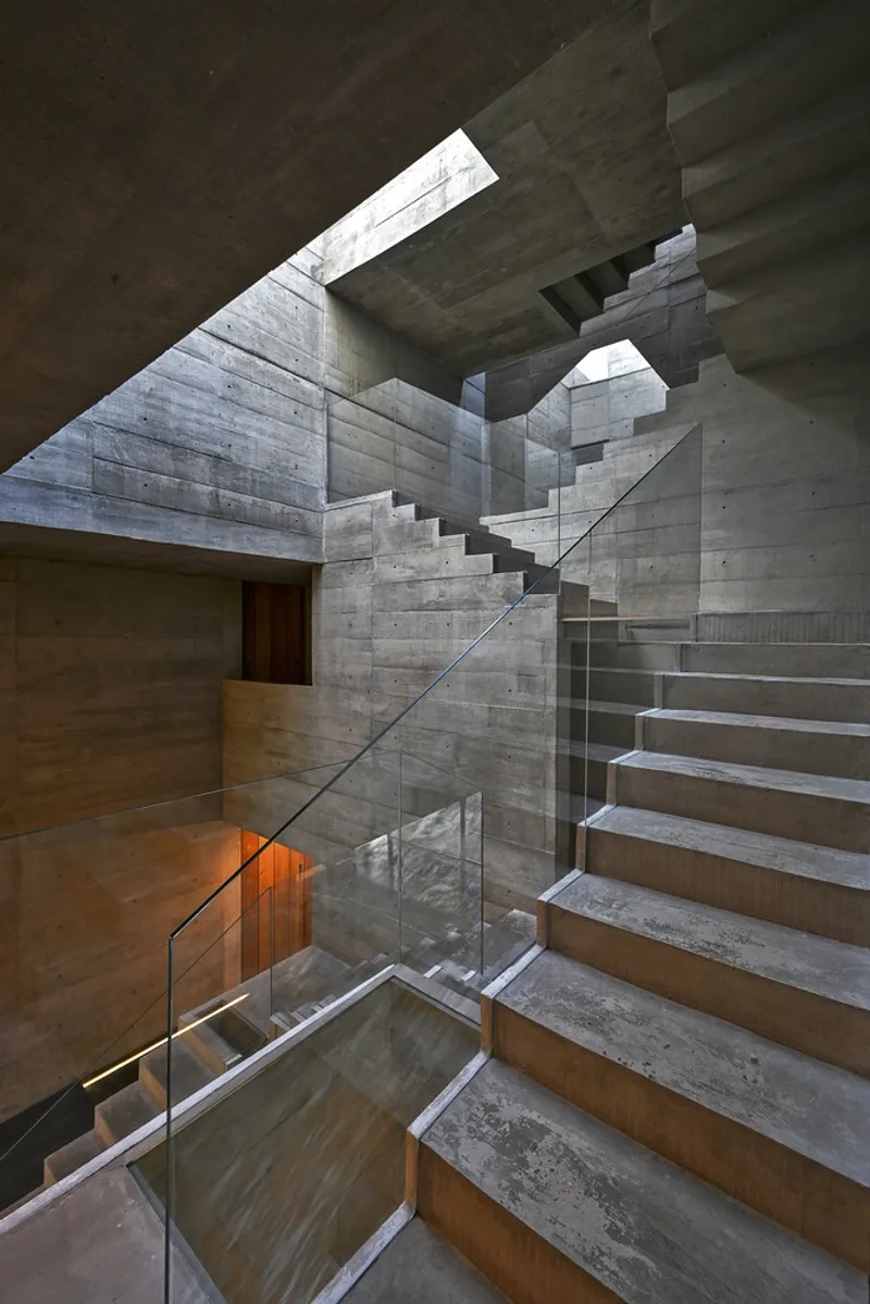 Multilevel board-formed concrete stairwell with angular skylights casting natural light on timber-clad steps