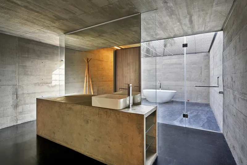Bathroom vanity in timber volume with glass enclosure separating sink area from freestanding tub under skylight