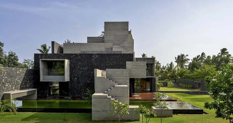 Garden view of stacked concrete volumes with external staircase and black stone cladding amid palm trees