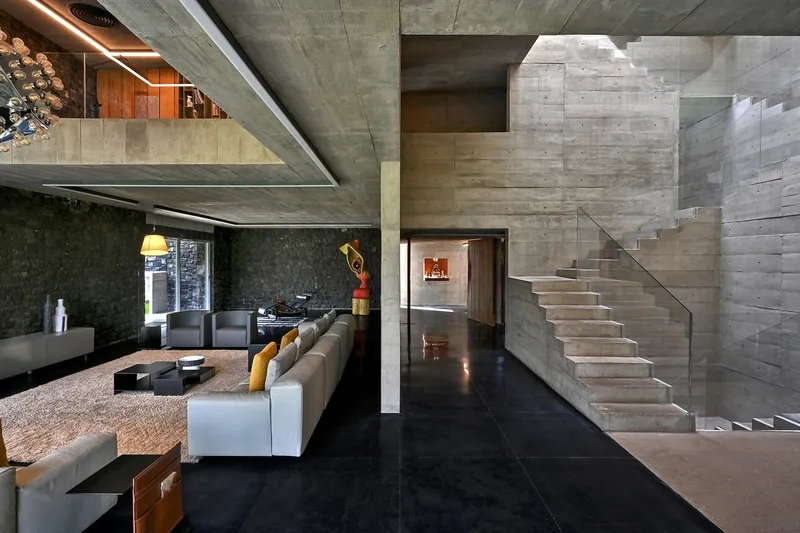 Double-height living space with concrete staircases and black polished floor beneath recessed ceiling