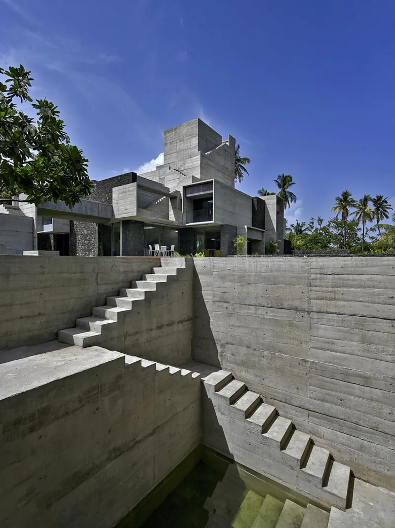 Sunken courtyard with board-formed concrete walls and cantilevered staircases under blue sky