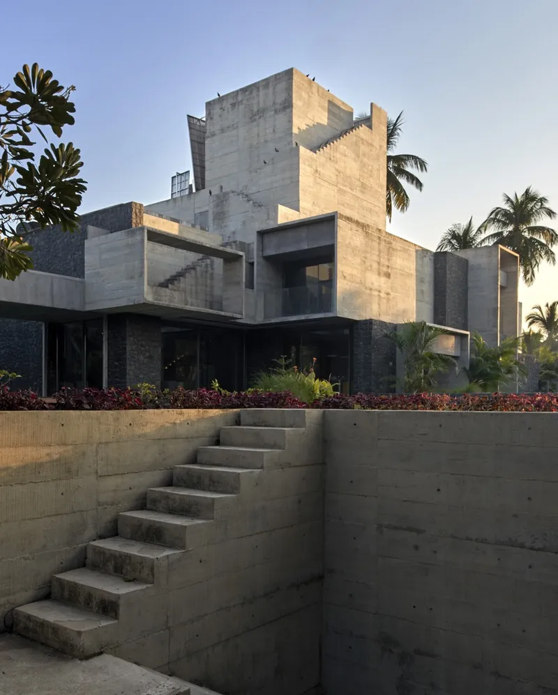 Board-formed concrete retaining wall with exterior stairs at sunset beside planted beds and palms