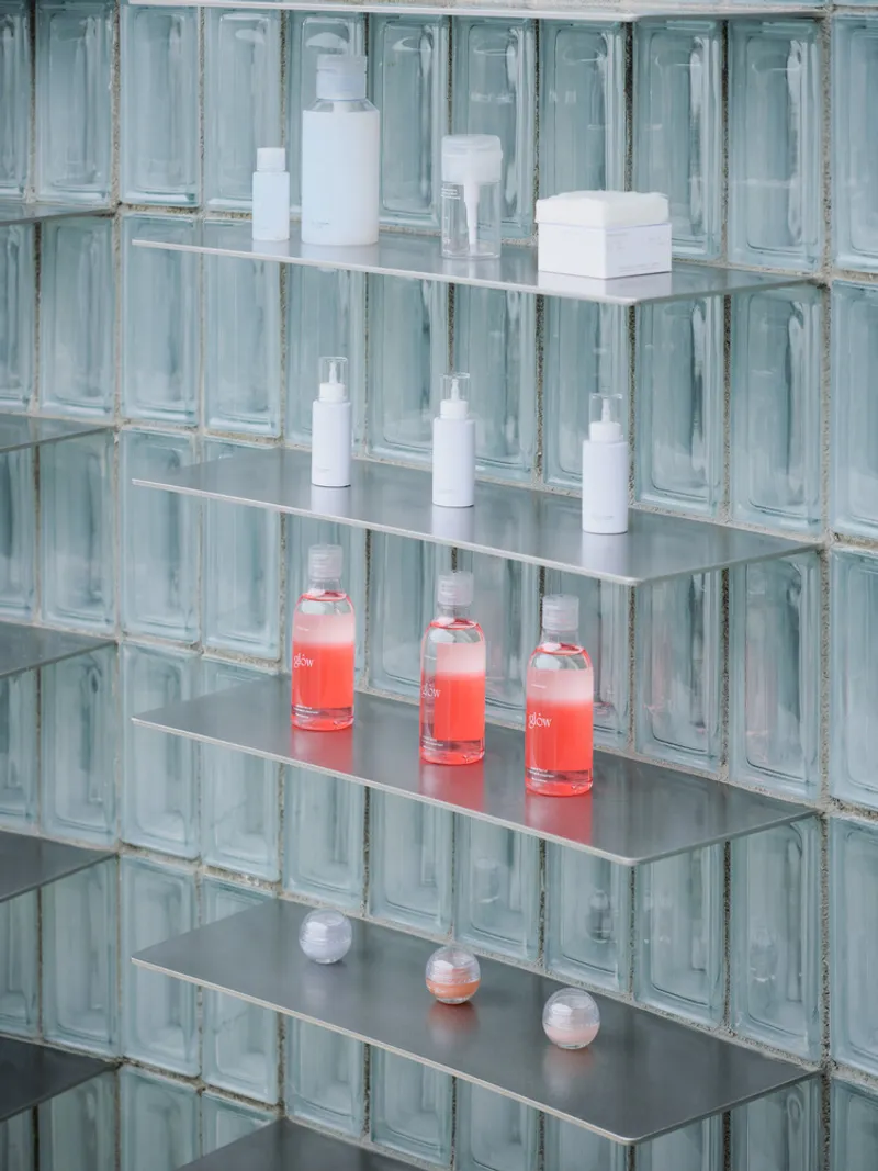 Close-up of glass shelving against glass block wall displaying cosmetic products in white and coral bottles