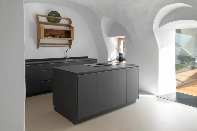 Black kitchen island beneath white vaulted arches with sunlight filtering through adjacent glazing