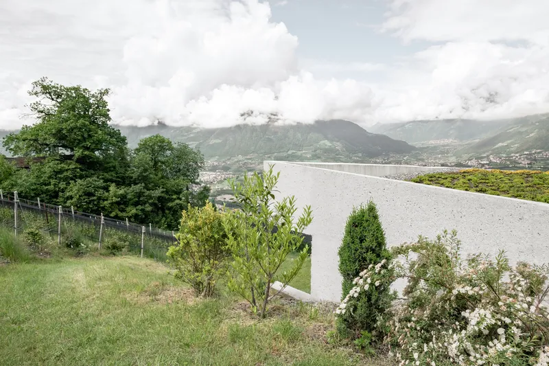 Concrete roof volume rising above planted slope with low clouds shrouding distant mountains