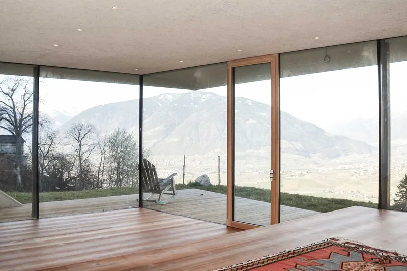 Interior view through sliding glass doors to timber deck and distant mountain range under overcast sky