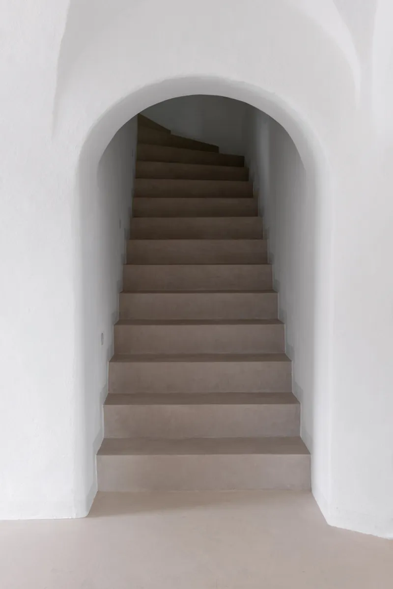 Curved stone staircase rising through arched white stucco passage with soft natural light