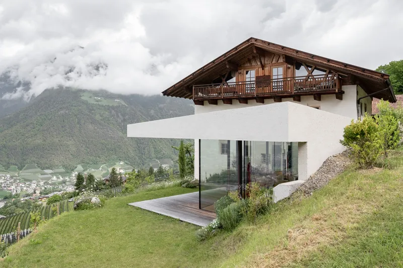 Hillside view of the timber gable roof with balcony atop the white extension overlooking valley and mountains