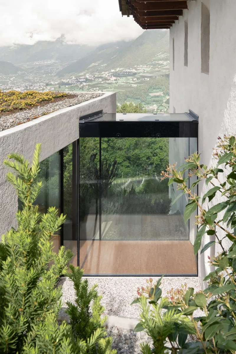 Glass corner window framed in black metal emerging from white stucco walls with gravel and plantings