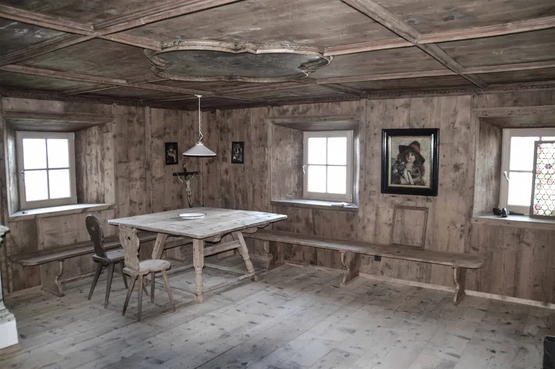 Timber-paneled room with coffered ceiling and central table beneath three small windows