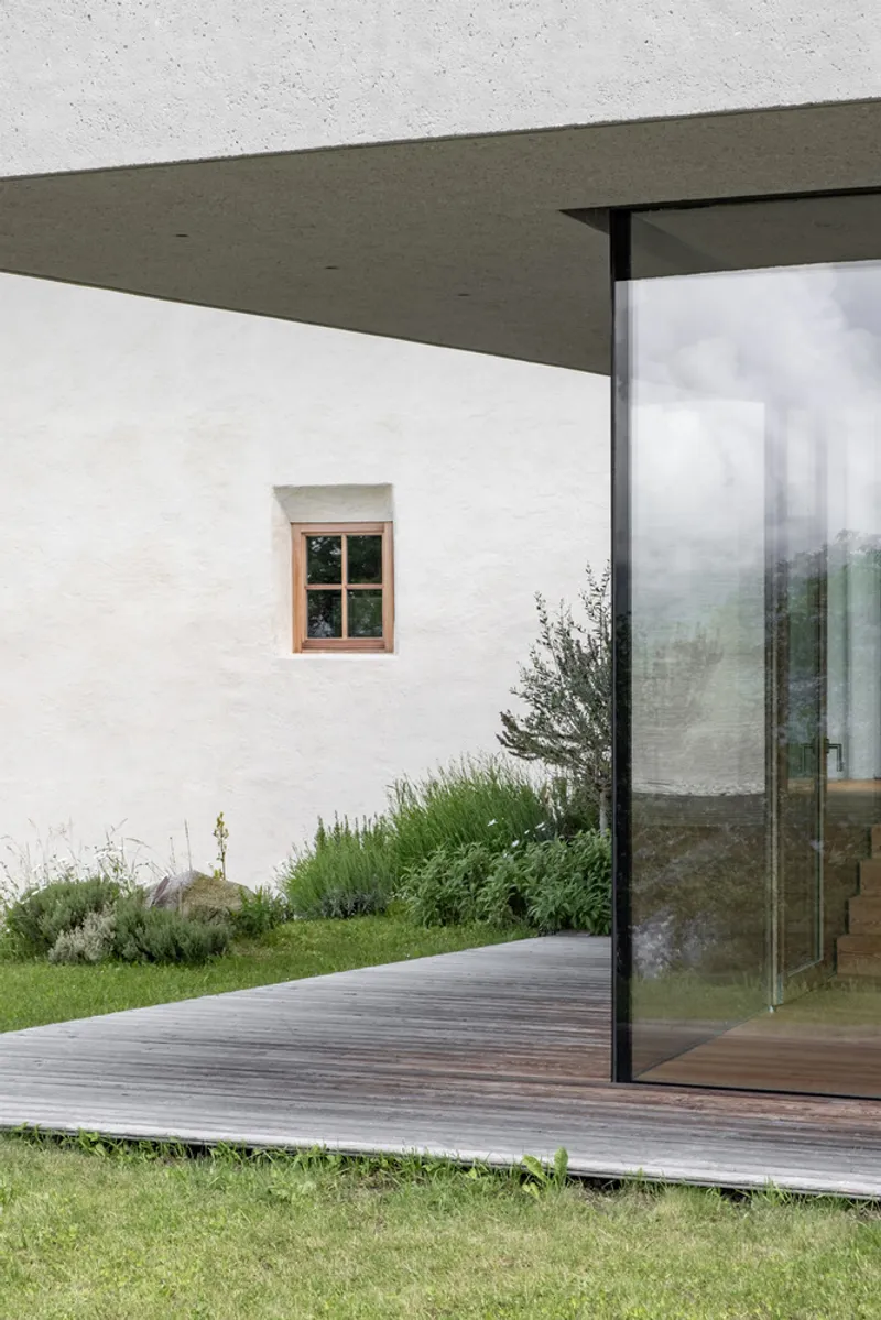 Timber deck terrace extending from glass walls beneath a flat concrete overhang in light mist