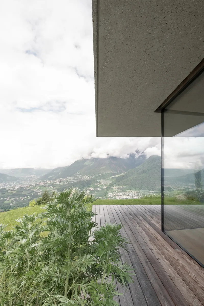 Covered timber deck with concrete overhang overlooking a valley settlement and misty mountains