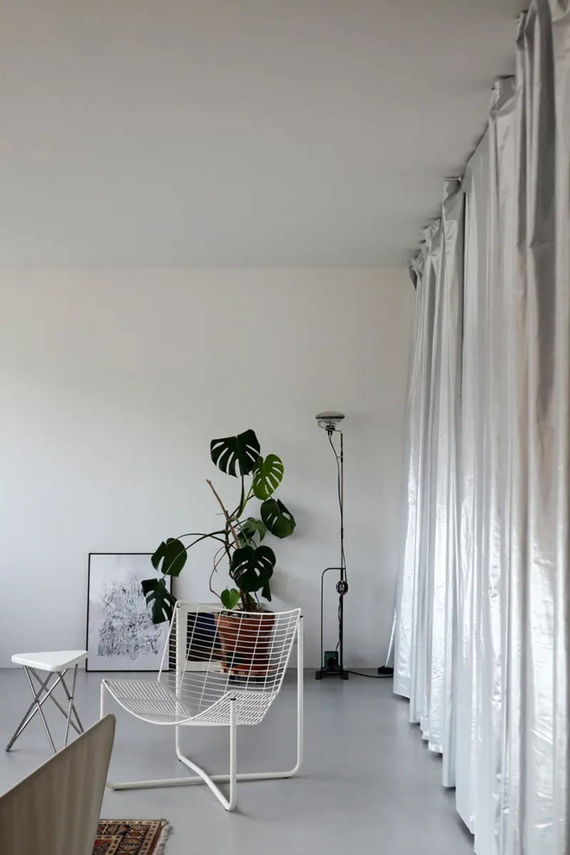 White wire chair with monstera plant next to full-height curtain and polished concrete floor