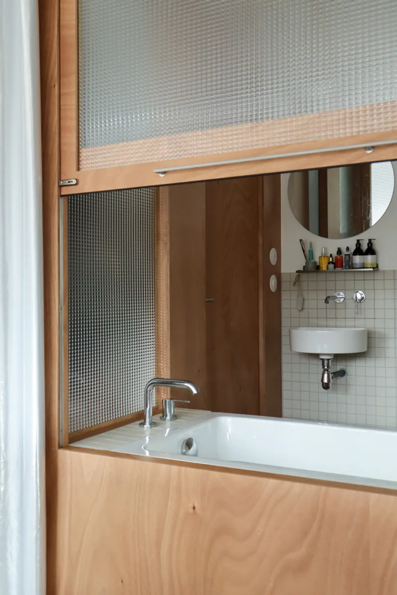 Bathroom alcove with built-in bathtub surrounded by timber cabinetry and reeded glass sliding panels