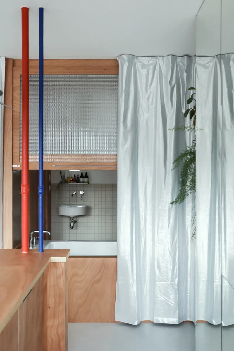 Kitchen nook with timber-framed reeded glass partition and exposed red and blue structural pipes