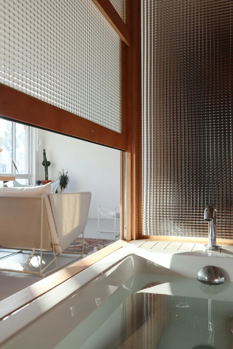 Bathtub beside timber-framed translucent glass panels with sunlight streaming through to the interior