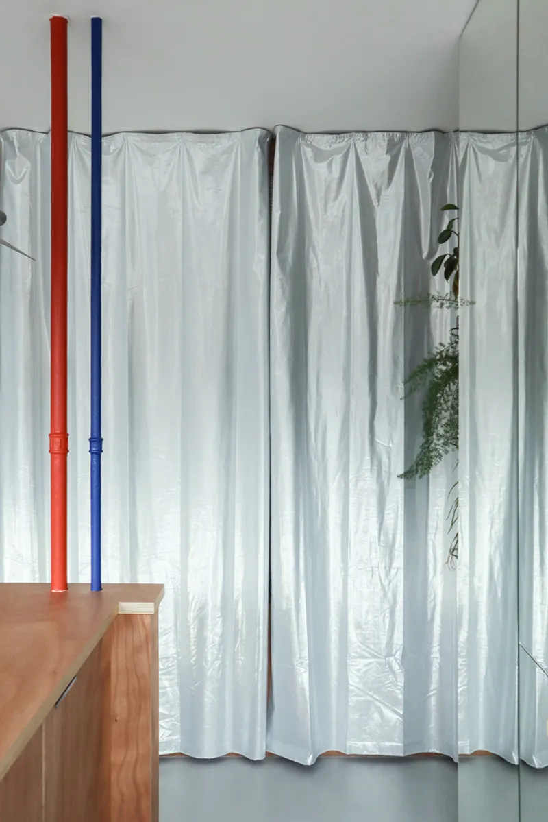 Floor-to-ceiling translucent fabric curtain with red and blue painted pipe columns and hanging plants