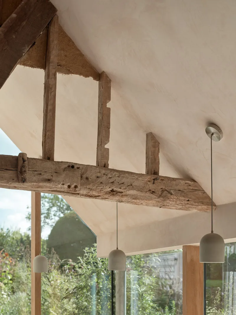 Vaulted ceiling with exposed timber beams and pendant lights above glazed openings to garden