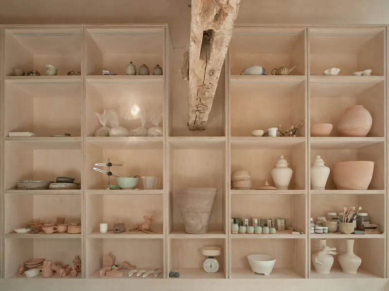 Plywood shelving unit displaying ceramic vessels and materials with a diagonal timber post passing through