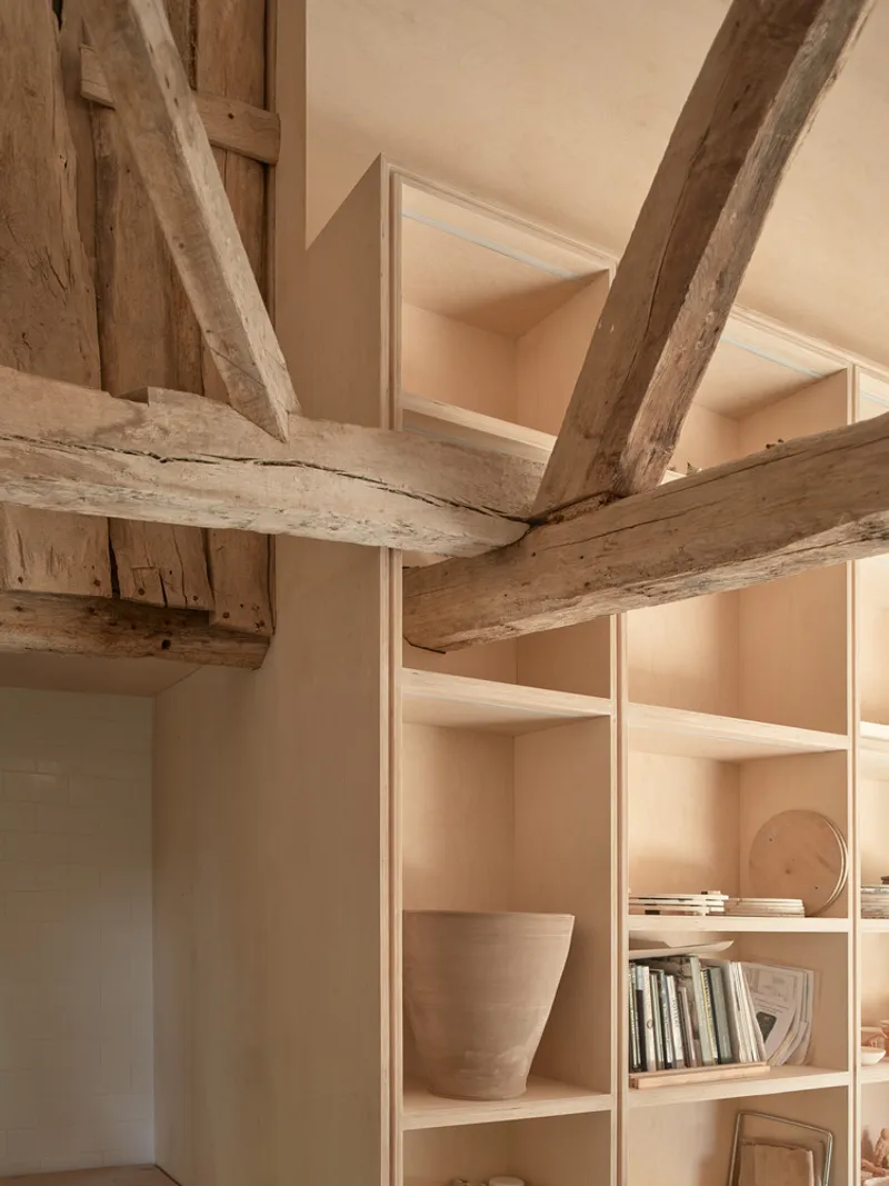 Corner detail showing exposed timber beams intersecting with built-in plywood shelving holding ceramic objects