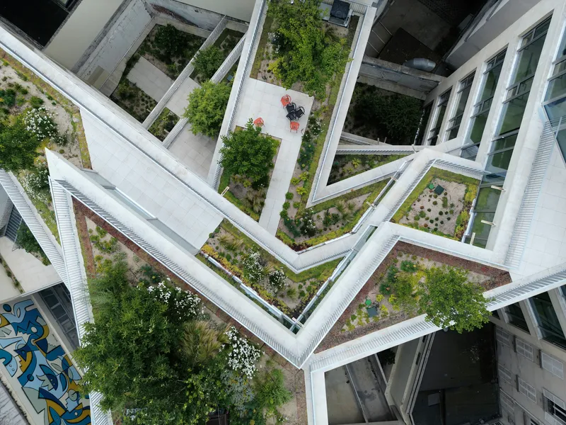 Aerial view of zigzagging white concrete roof beams framing green roof terraces with planted beds and trees