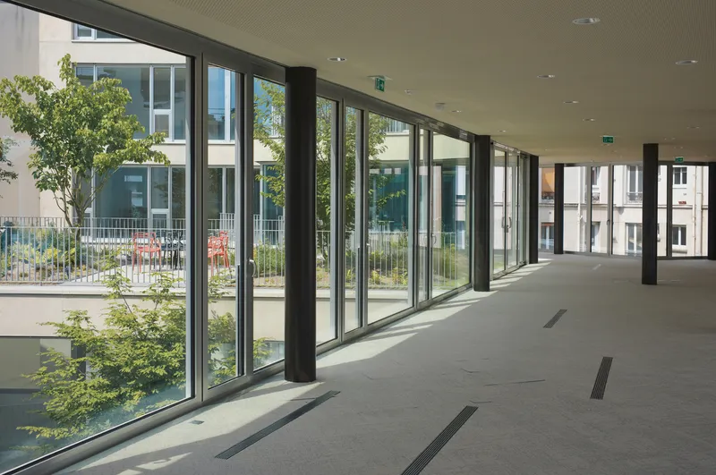 Interior corridor with full-height glazing, circular black columns and a view to the planted terrace beyond