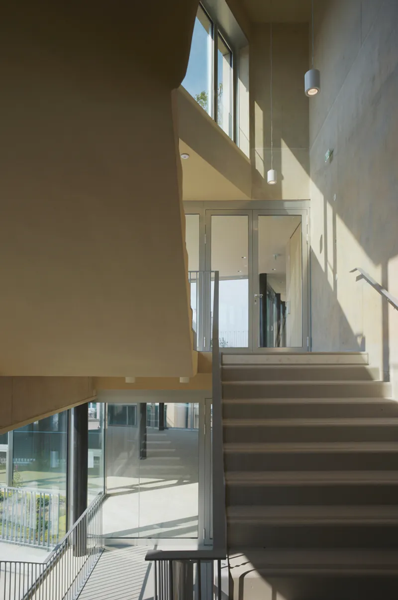 Multi-level stairwell with glass elevator shaft and clerestory windows casting sharp afternoon shadows