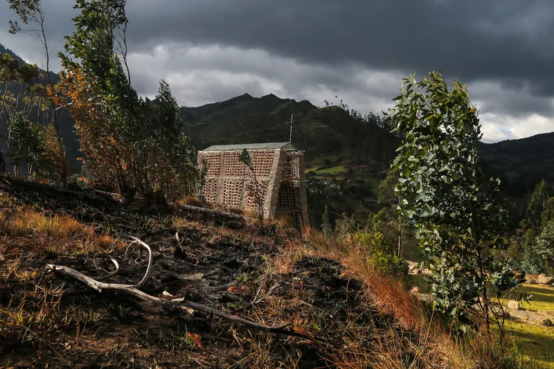 Perforated brick structure on a burnt hillside under dark storm clouds