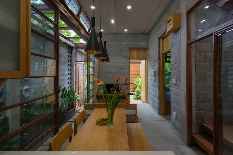 Dining area with timber framed windows, concrete block walls, and clerestory openings filtering daylight through foliage