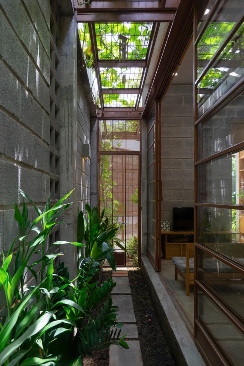 Narrow courtyard slot with concrete block walls, timber framed skylights, and planted bed along stepped pavers