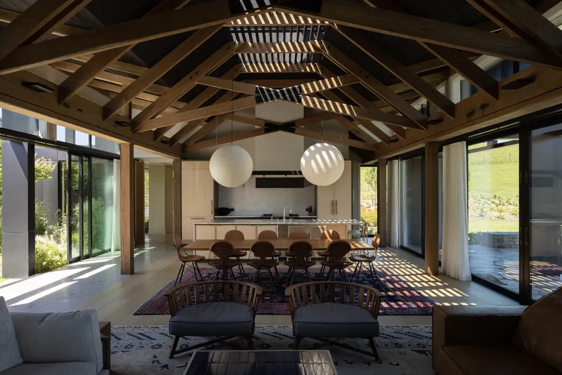 Open-plan dining area with exposed timber roof trusses and dappled sunlight across the floor