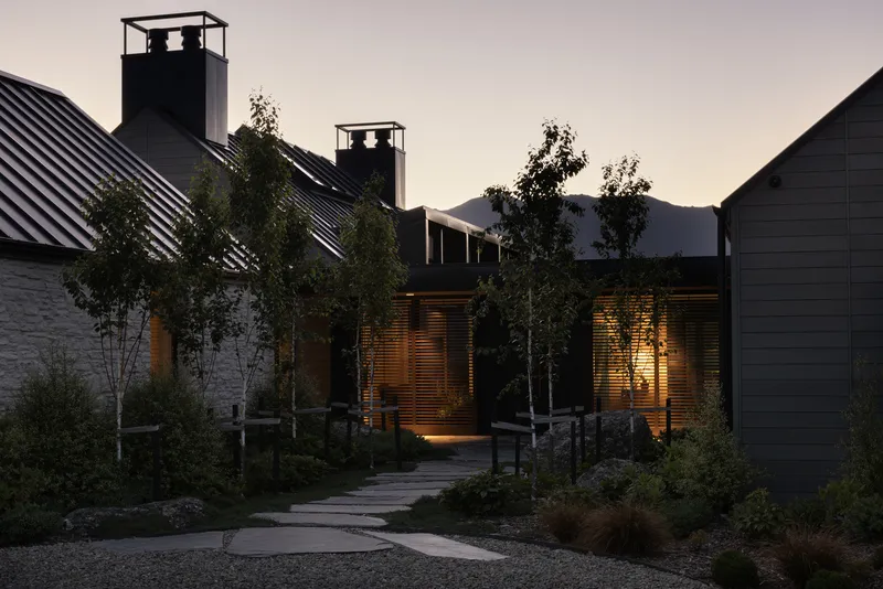 Entry path lined with young birch trees leading to louvered doors at dusk