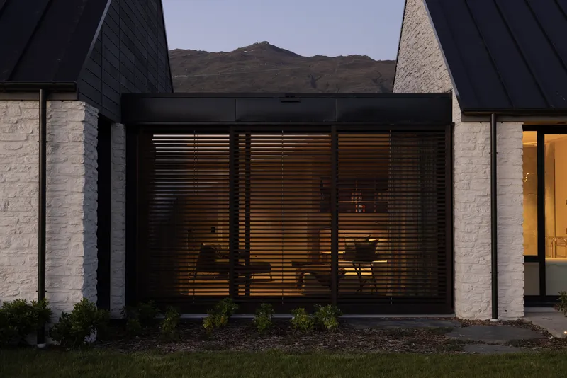 Close-up of horizontal timber louvers between painted masonry and dark cladding at twilight