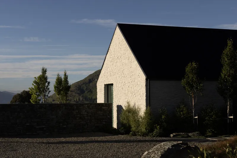 White painted brick gable with standing seam roof behind a low stone wall at dusk