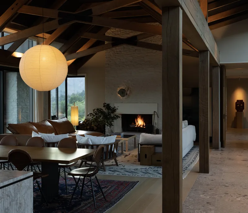 Open-plan living area with exposed timber beams, fireplace, and spherical paper pendant light at dusk