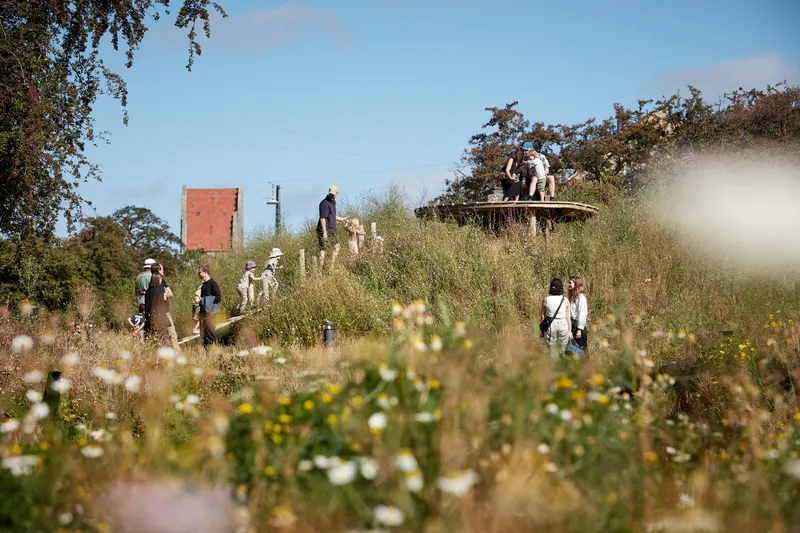 Visitors walking through the wildflower meadow with a viewing platform and brick building in the distance