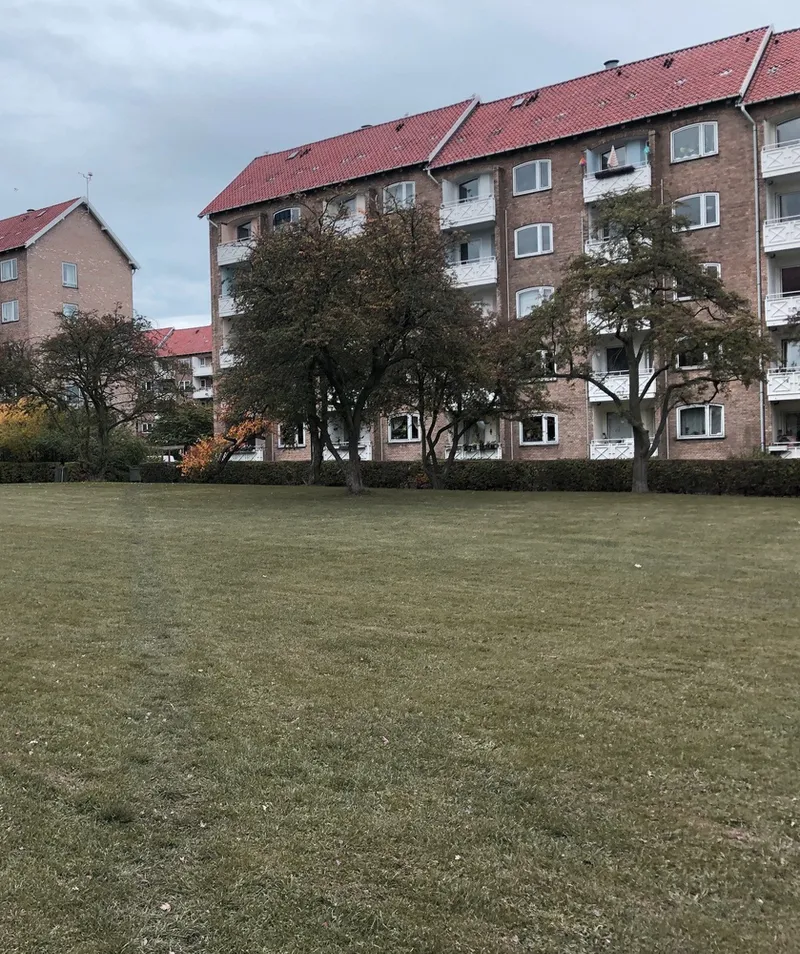 Brick housing block with red tile roof and balconies beyond mowed grass and leafless trees