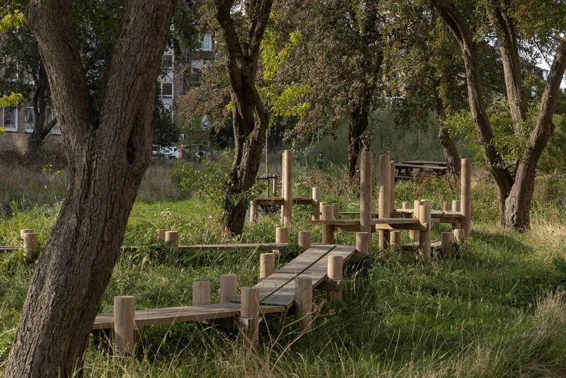 Timber play structure with posts and platforms winding through an open green space among mature trees