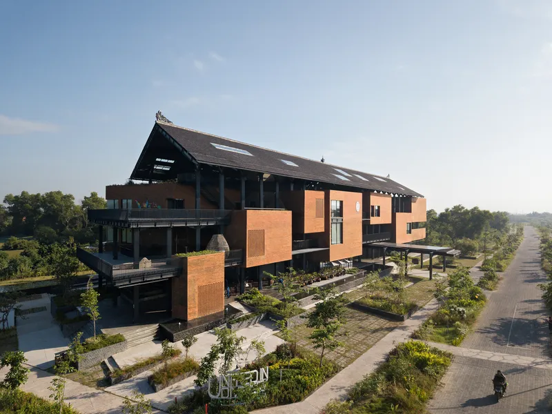 Elevated view of the orange brick clad volumes beneath the overhanging dark roof surrounded by landscaped pathways