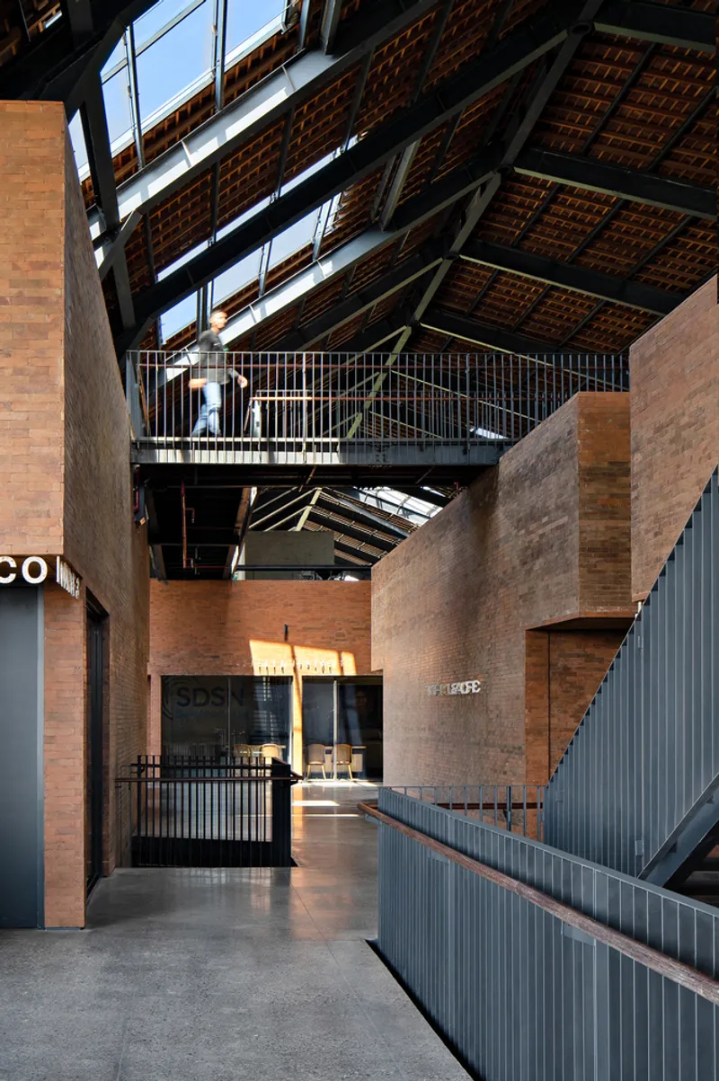 Triple-height interior atrium with exposed timber roof trusses and steel walkways connecting brick volumes
