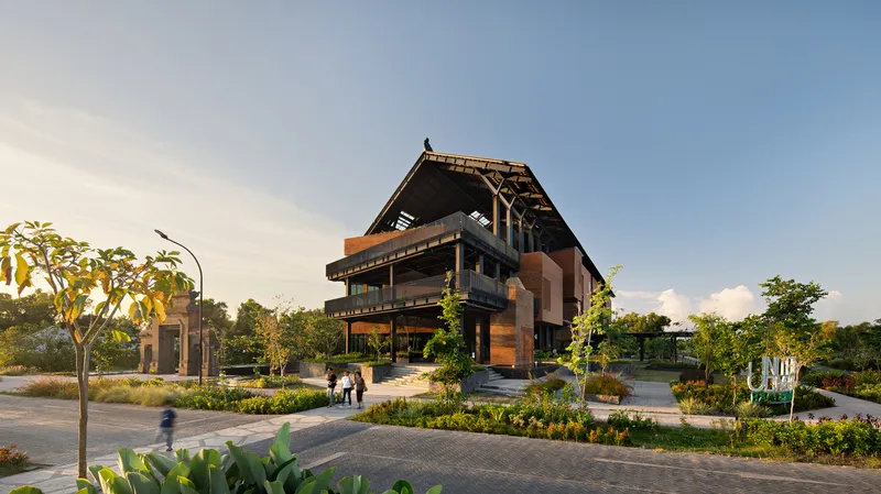 Corner view of the building at dusk with pedestrians on pathways beneath young trees and plantings