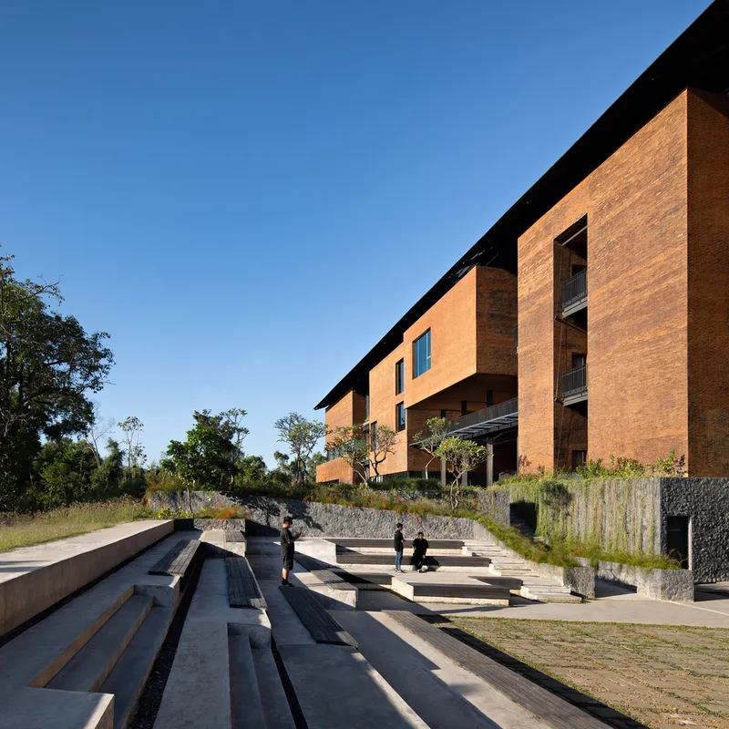 Terraced concrete amphitheater steps leading up to elevated rammed earth buildings with scattered visitors below