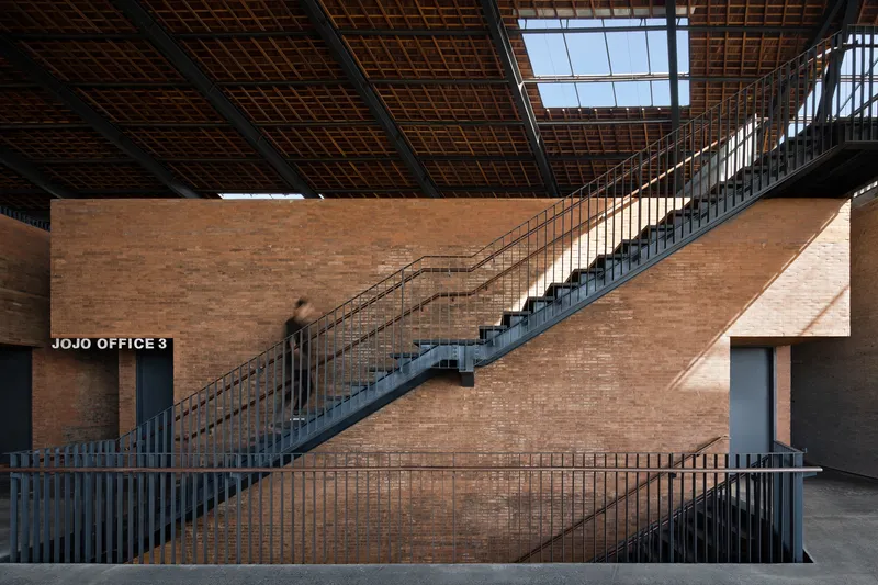 Steel staircase with railings spanning across a rammed earth wall beneath skylights in the timber ceiling