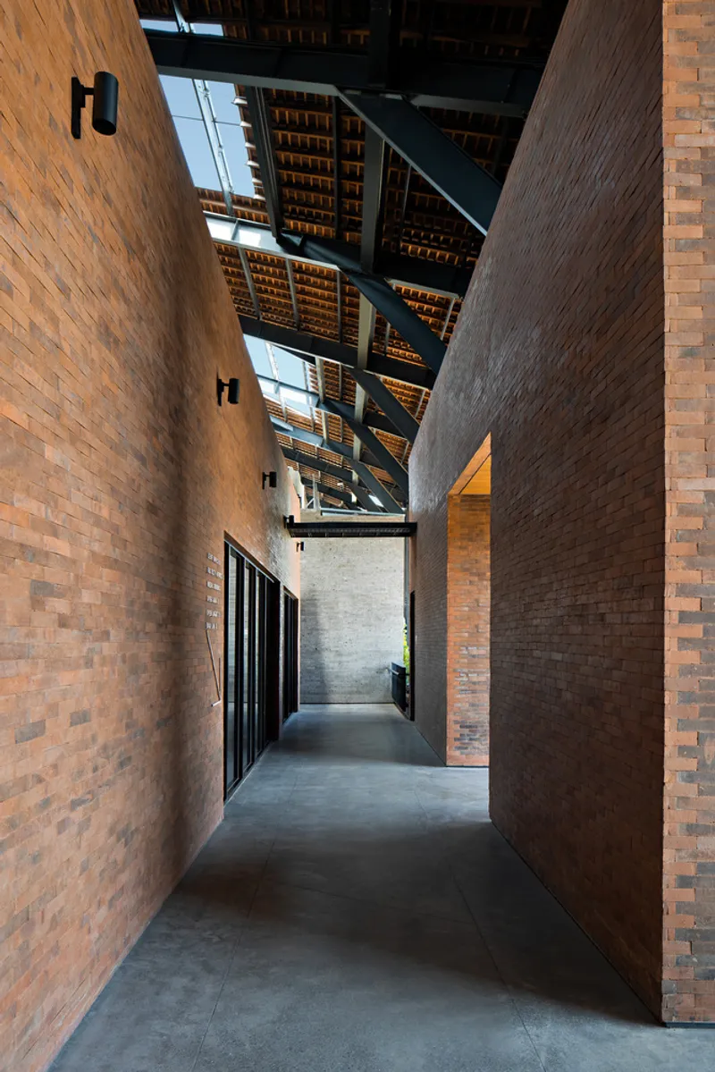 Corridor between tall rammed earth walls with overhead steel framing and clerestory glazing above